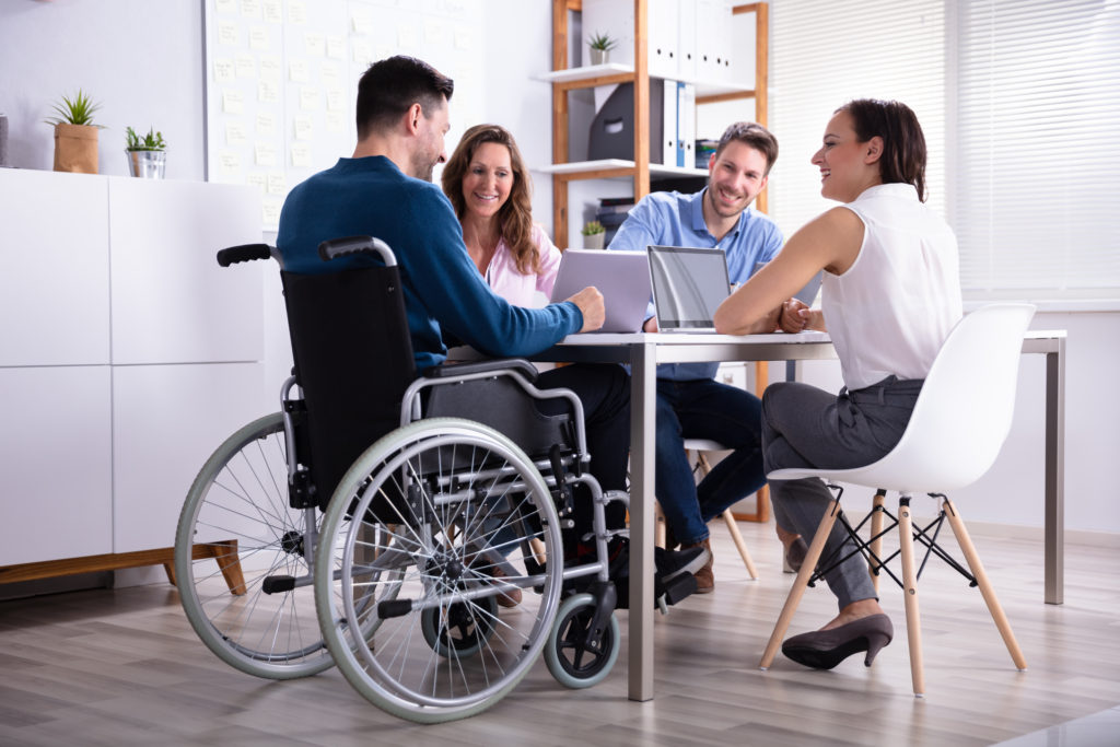 Disabled Male Manager Sitting With His Colleagues At Workplace