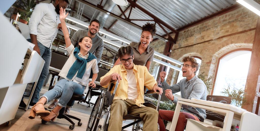Does work make you happy? Young positive asian man in wheelchair having fun with his colleagues at modern office