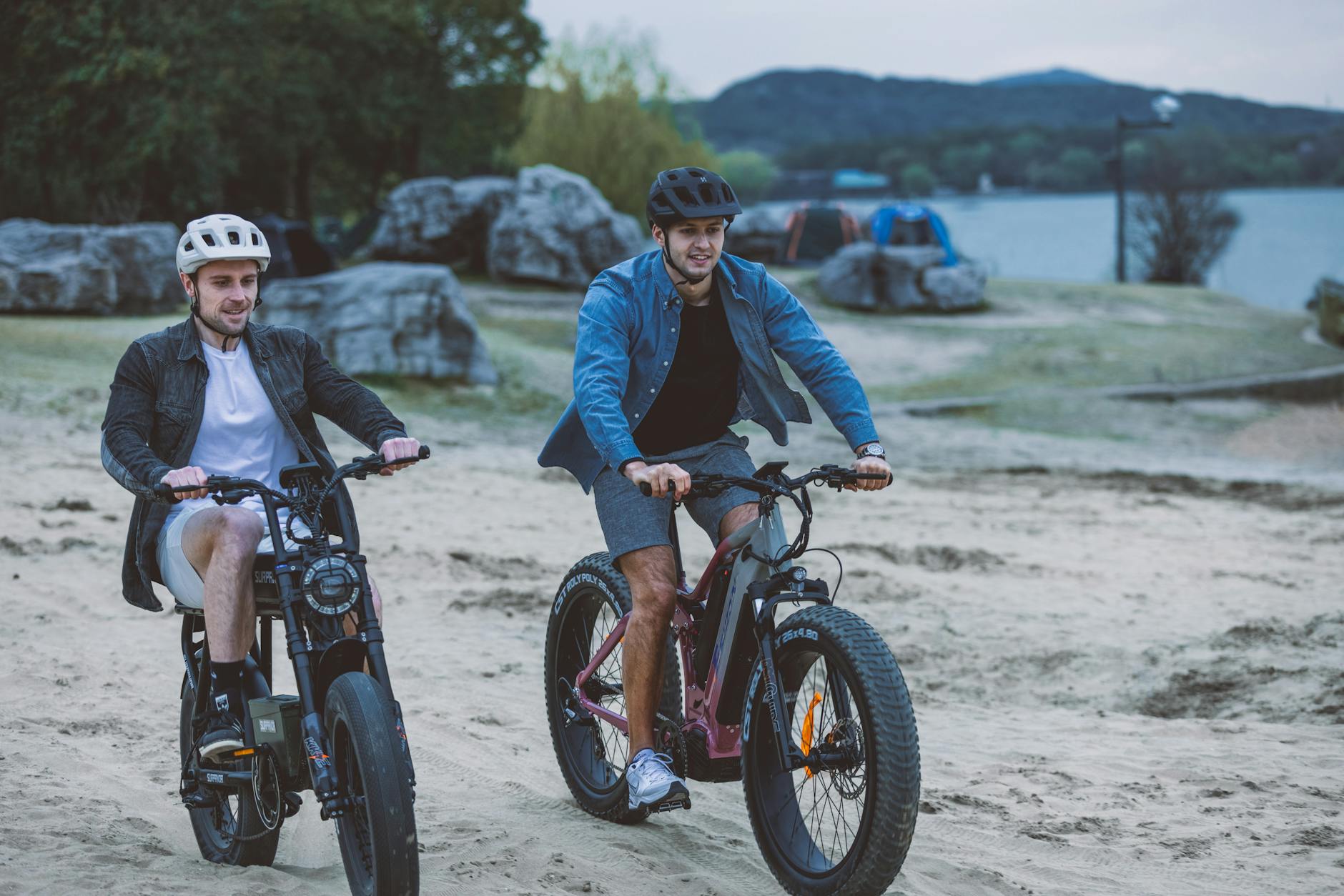 two young men riding electric bikes on sand