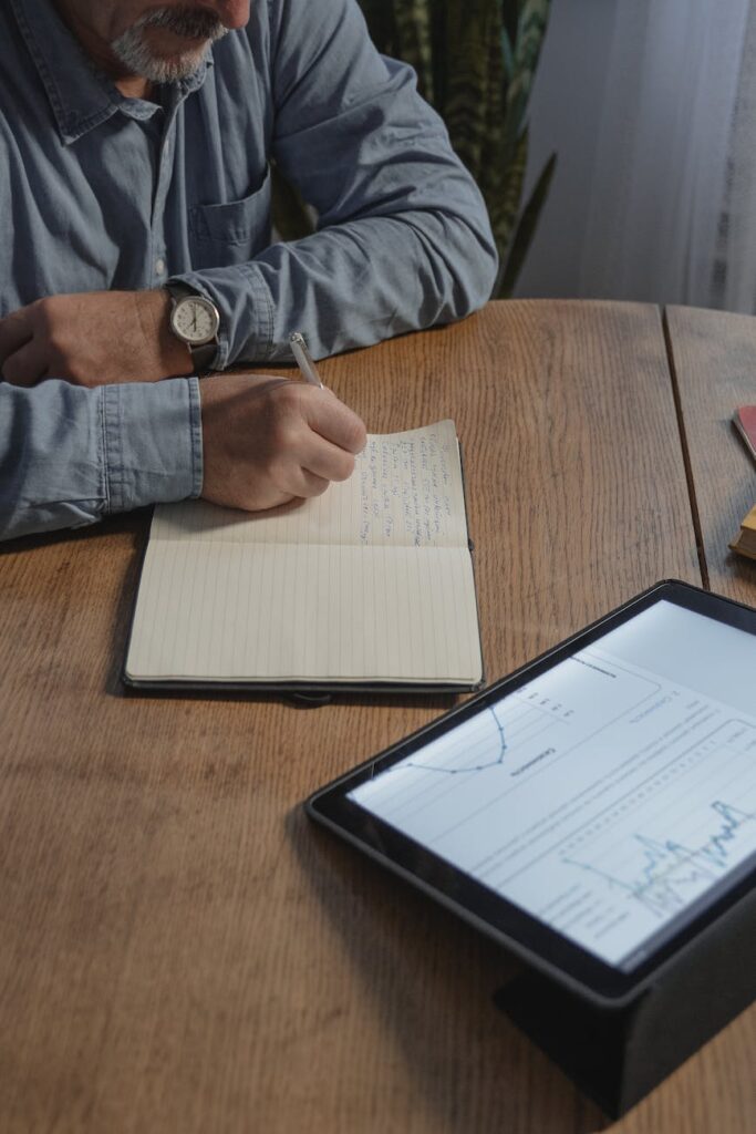 man writing on a paper with data analysis study in an ipad