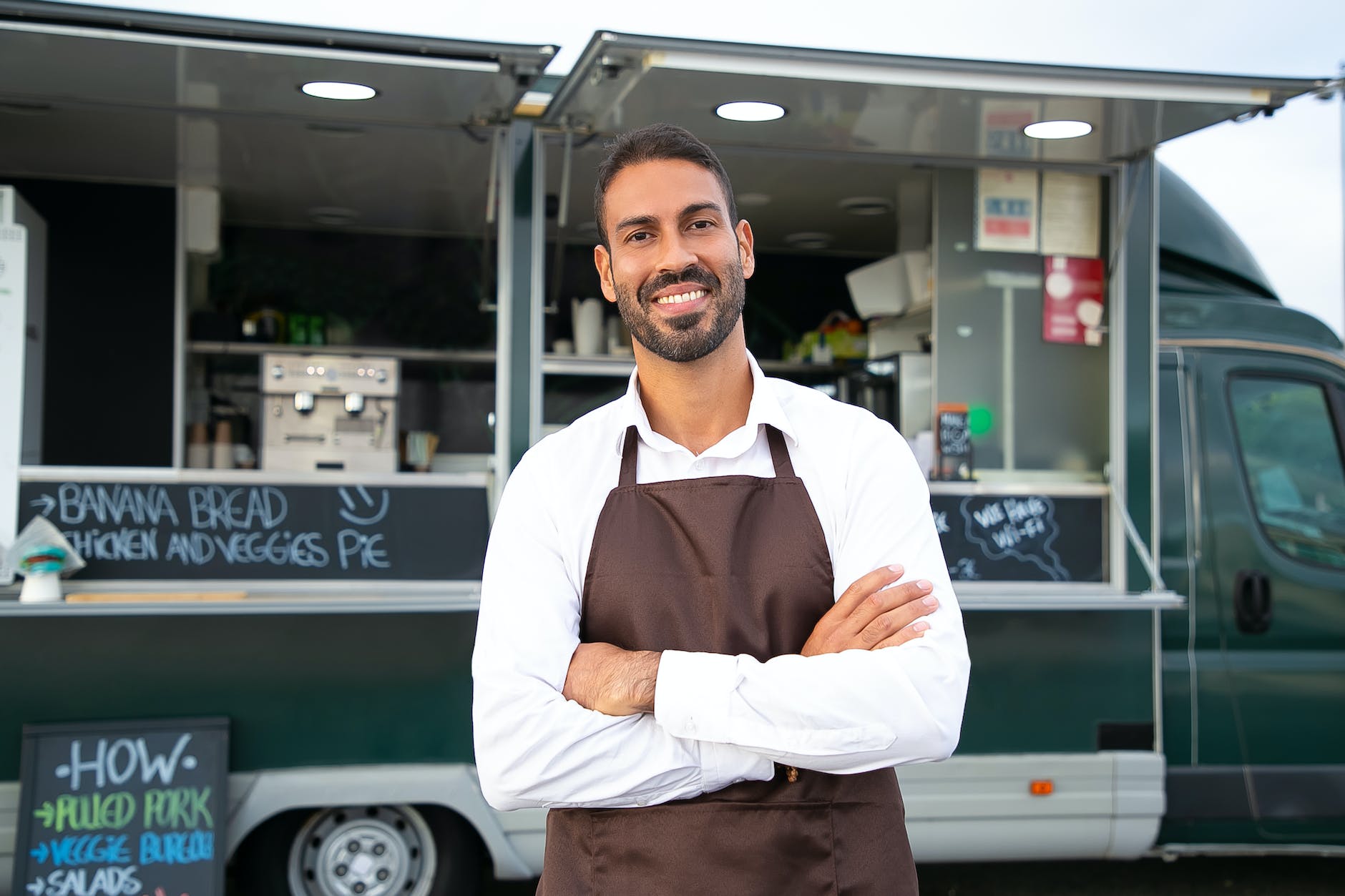 cheerful ethnic male food truck waiter standing with crossed arms