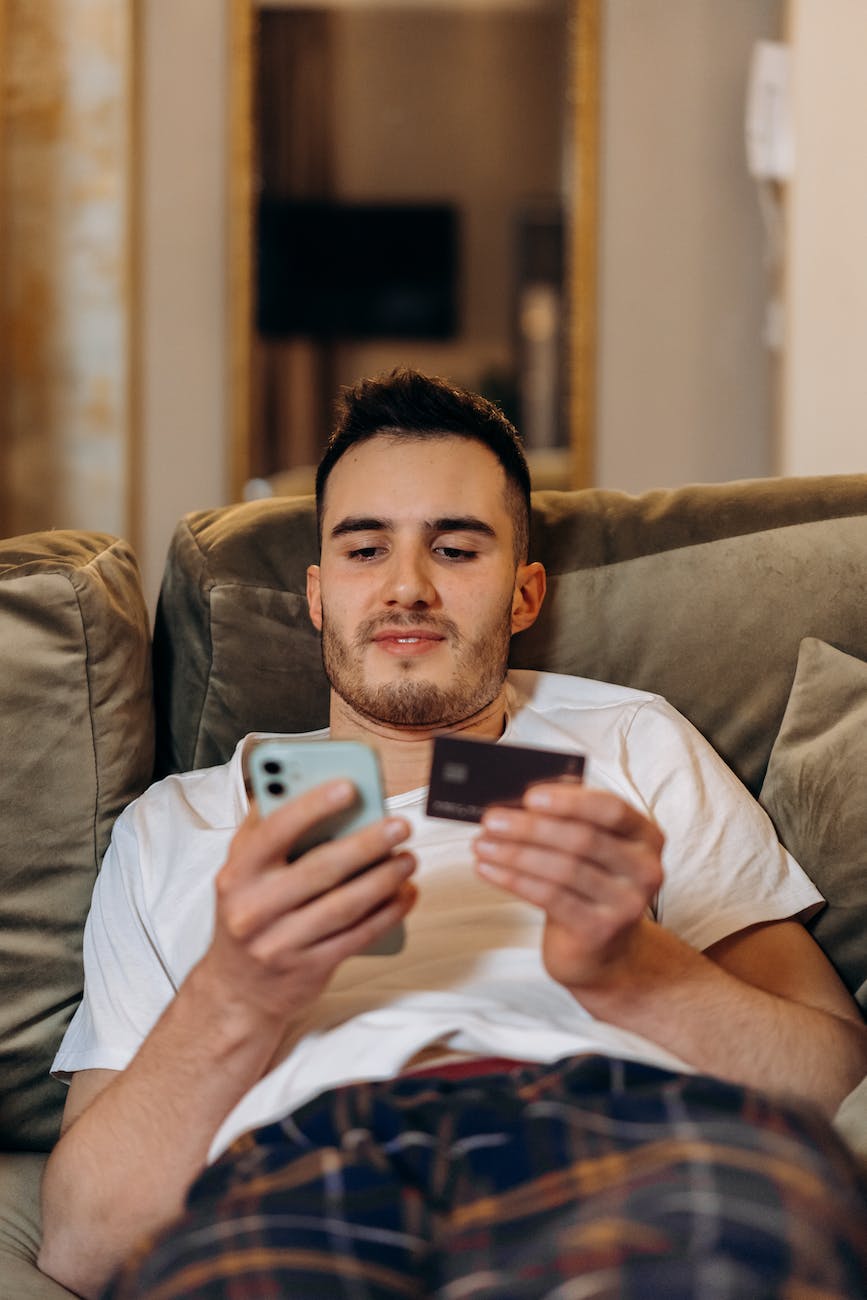 man laid back on a couch holding a smartphone and card