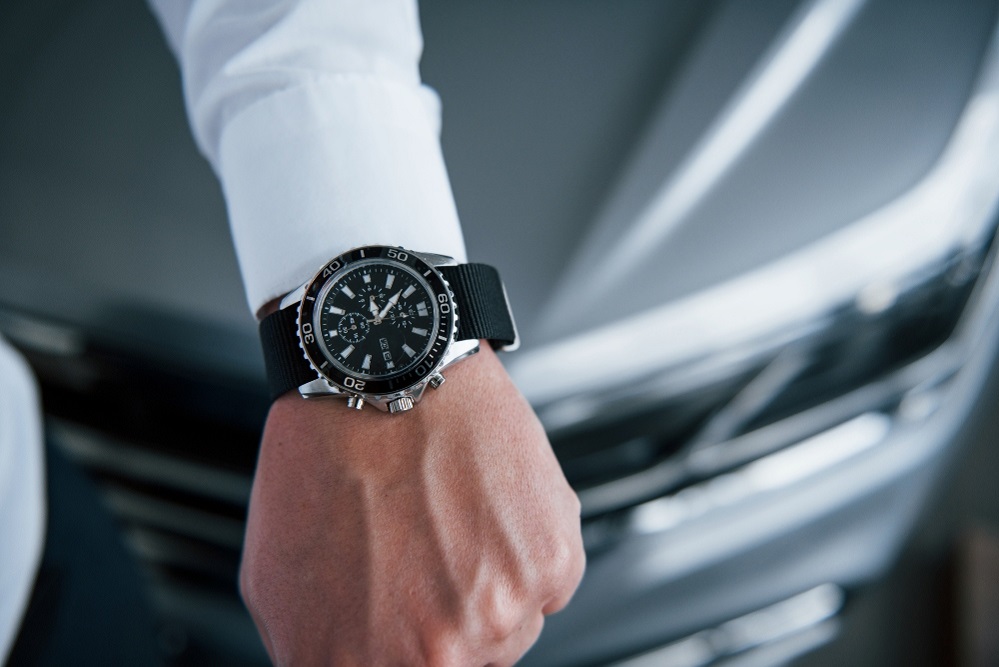 Close up photo of man's hand in suit with luxury watch near the car.