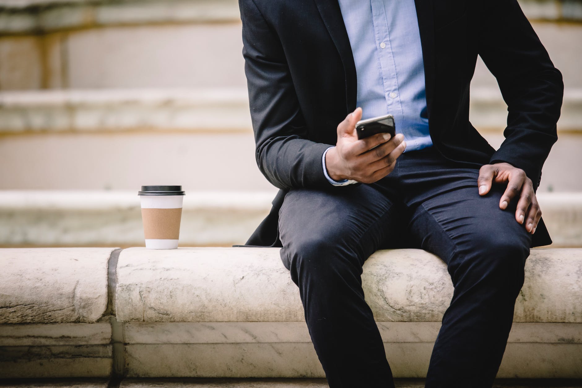 crop businessman using smartphone while resting on bench with takeaway coffee