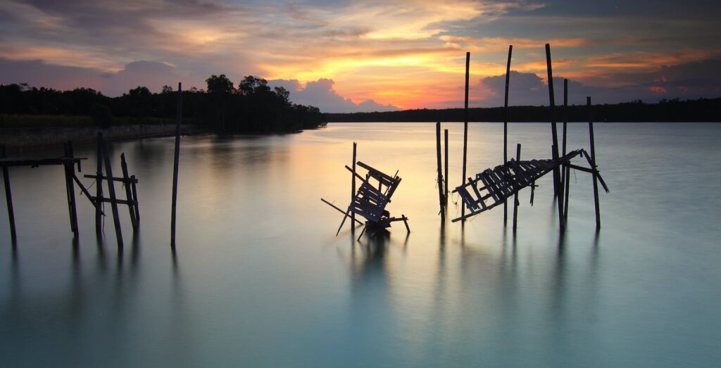 silhouette of broken boardwalk on body of water under sunset