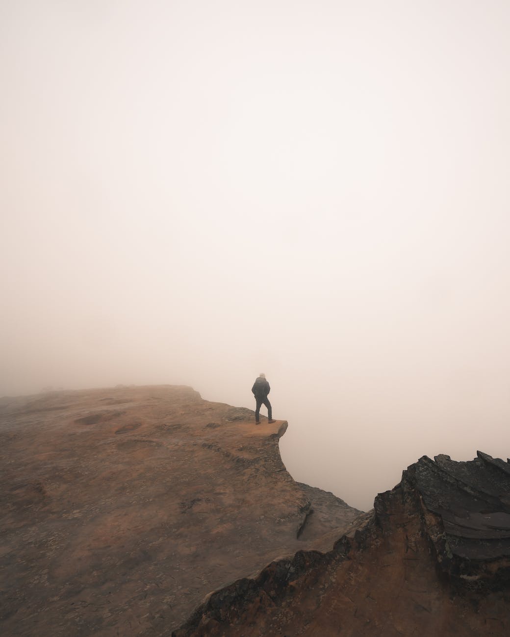 person standing on a cliff during foggy weather
