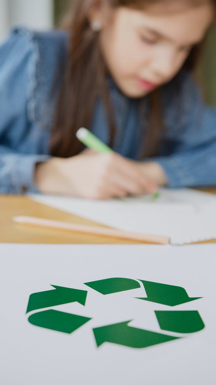 paper with green recycle logo on table across a girl studying about recycling