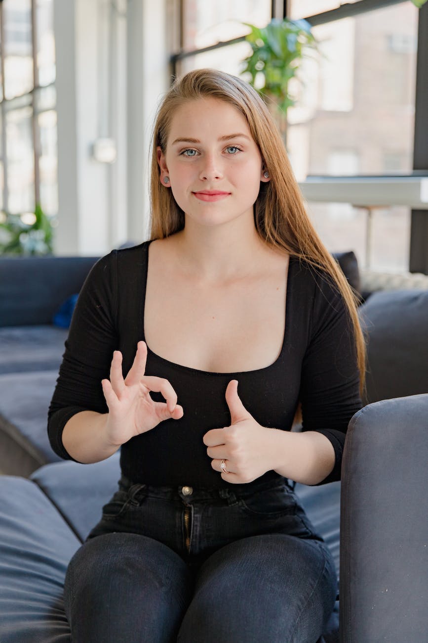 portrait of smiling woman sitting on sofa showing sign language