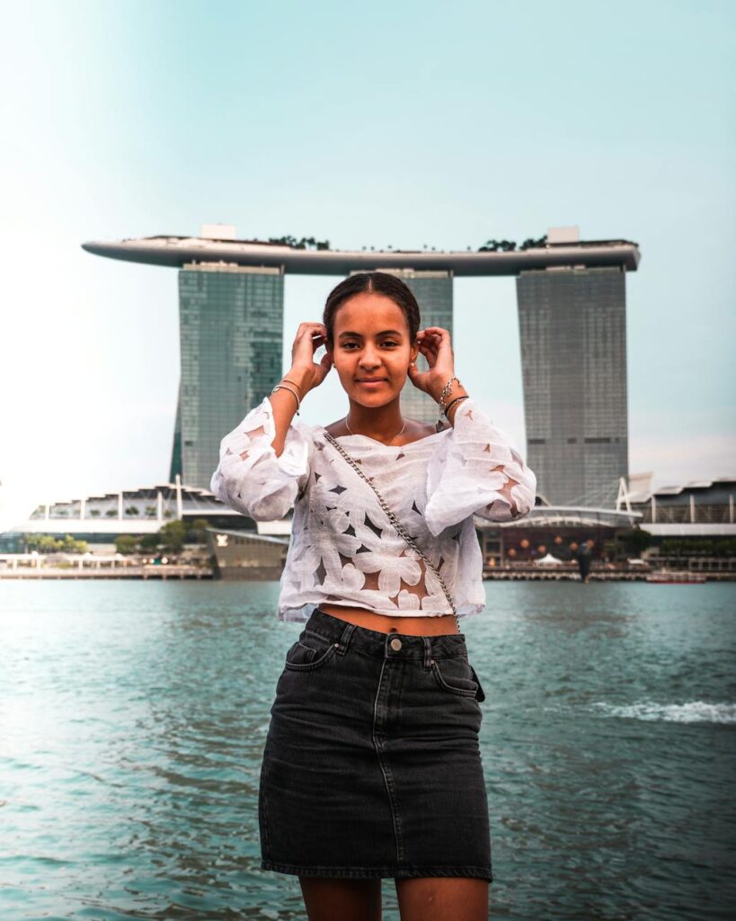 photo of smiling woman in white top and black denim skirt standing with the marina bay sands resort in the background