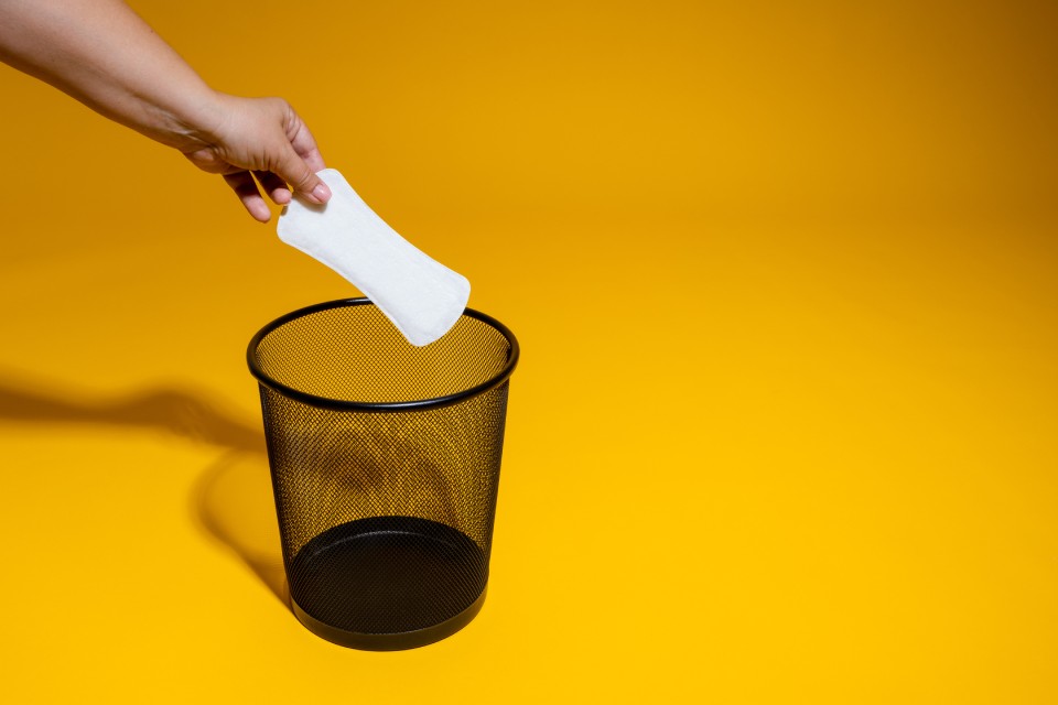 A woman’s hand holding a sanitary pad over an empty disposal bin.