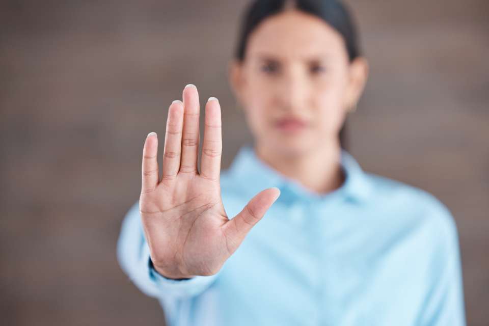 A woman wearing a blue business shirt holds out her hand directly forward, with the focus on her hand.