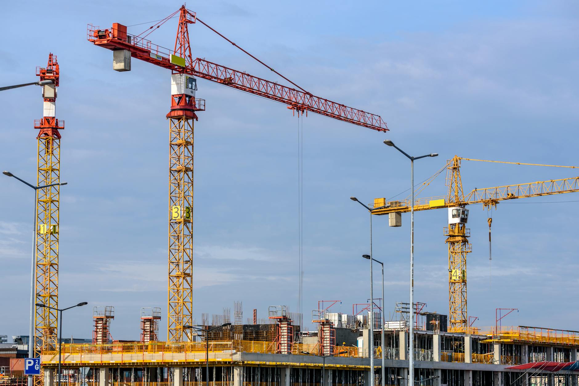 three yellow and red tower cranes under clear blue sky