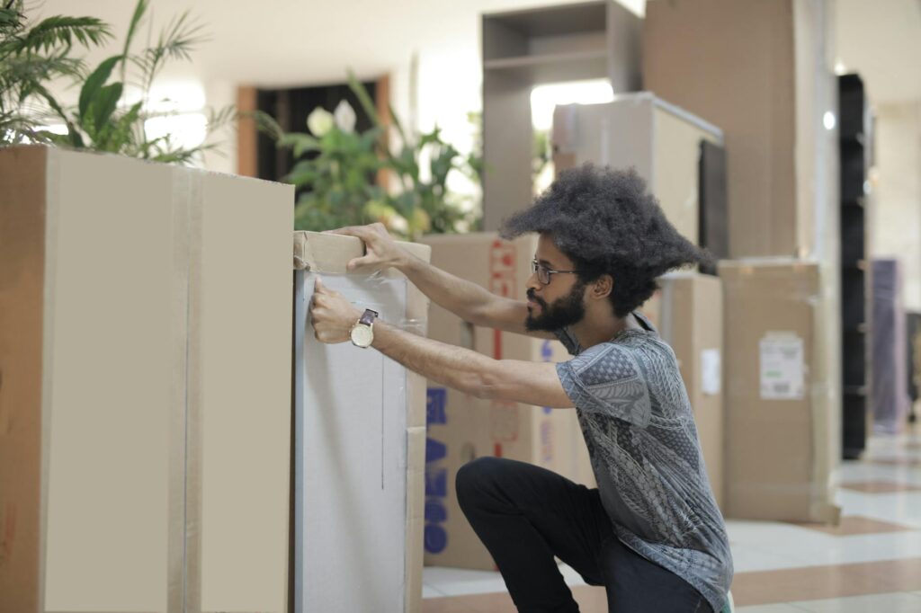 ethnic man closing boxes in corridor of modern office
