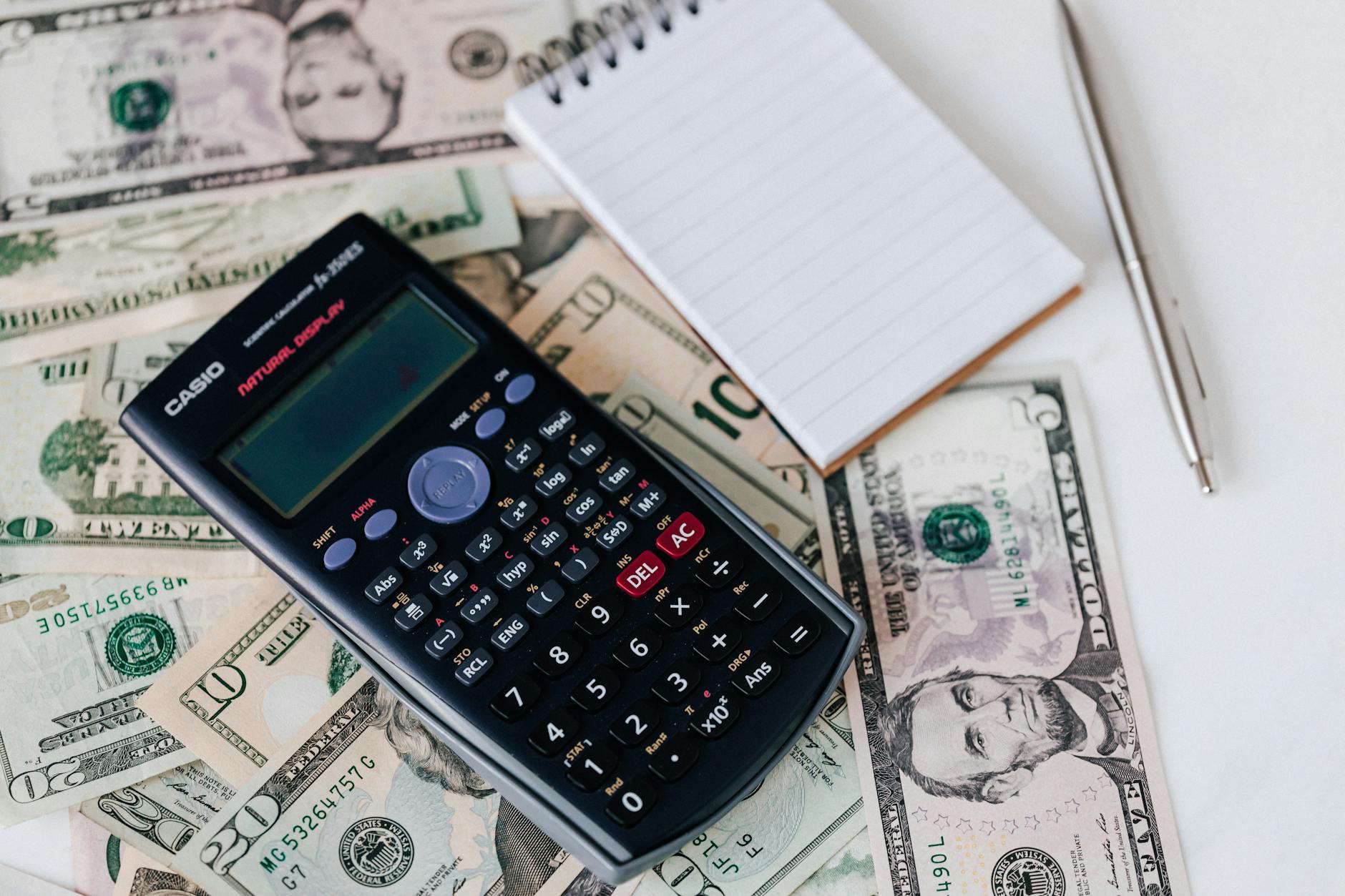 calculator and notepad placed on usa dollars stack