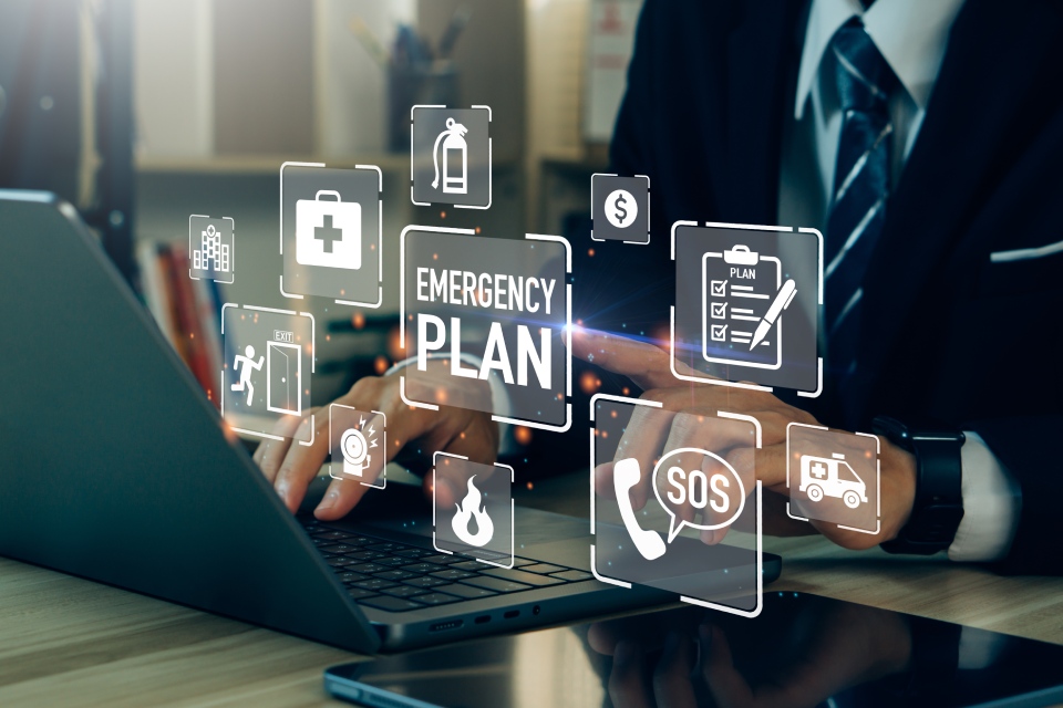 A businessman at his laptop, pointing at a graphic above it that says "emergency plan." There are other graphics surrounding it.