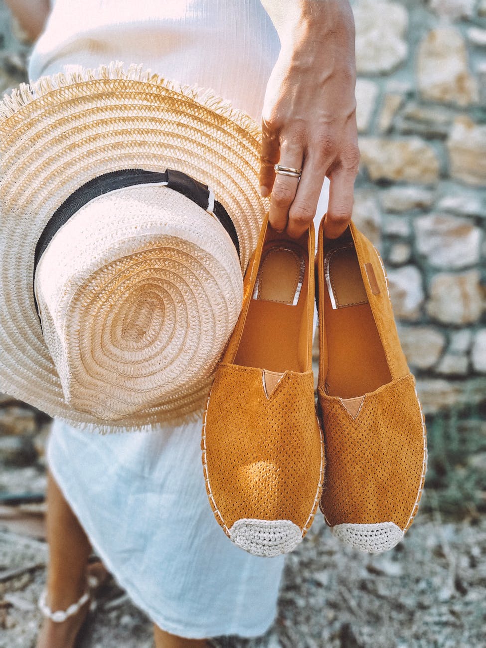 selective focus photography of woman holding brown espadrille shoes and brown sun hat