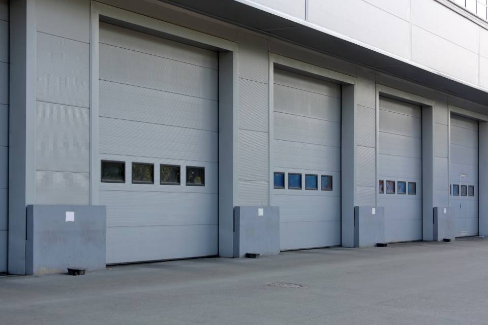 Four loading bay doors are positioned next to each other. The doors are gray and have small windows in the center.