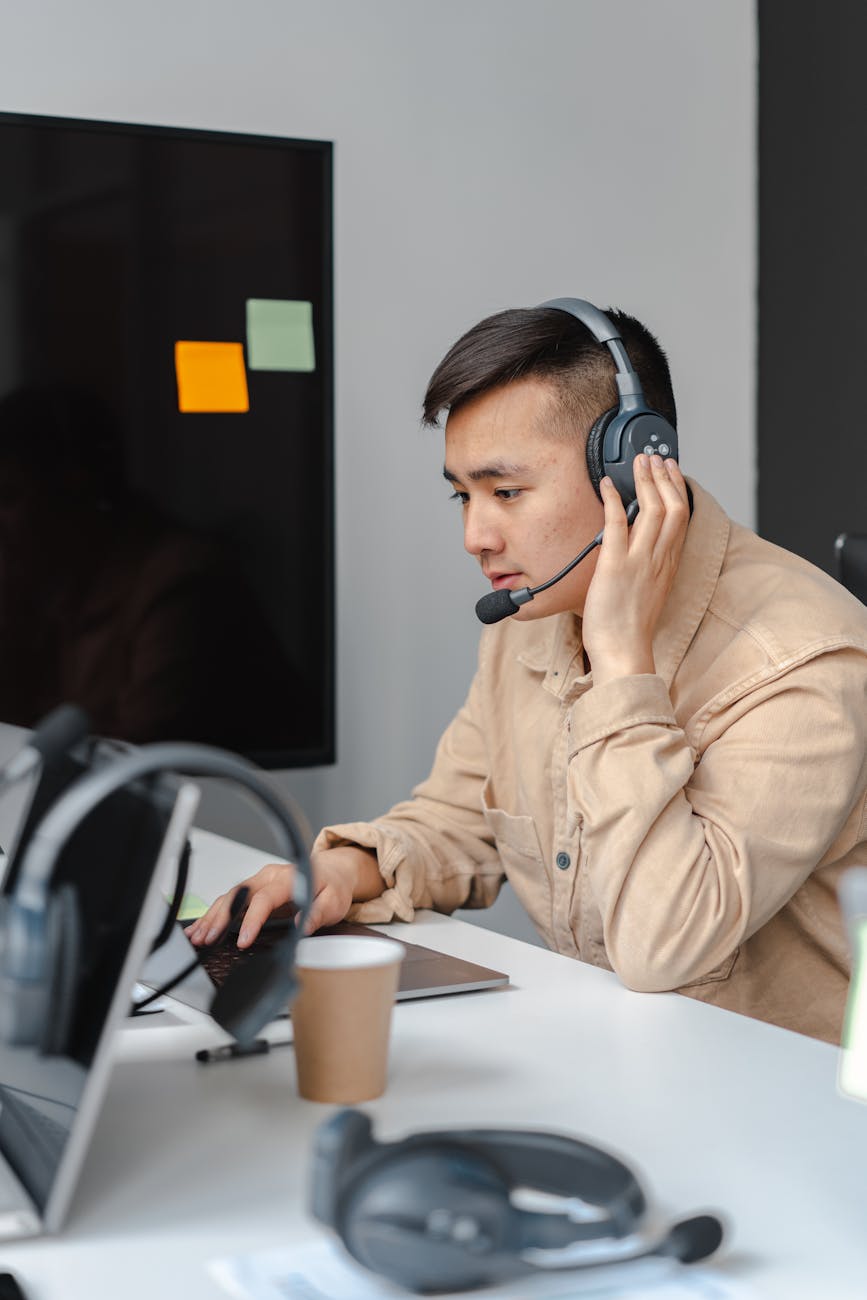 a man talking on a headset while using a laptop