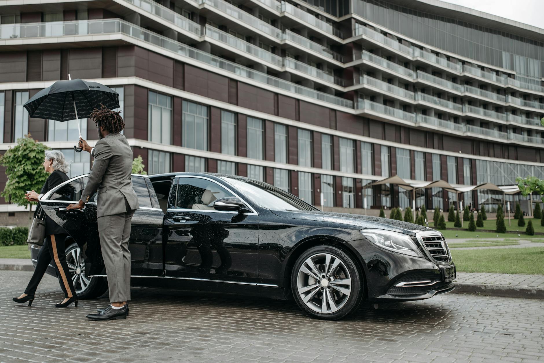 man in gray suit standing beside a black car