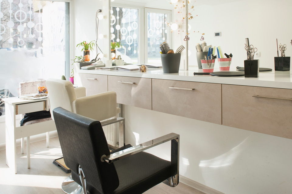 A hair salon in a smaller space. There are only a few chairs with a mirror in front of them and a window letting some light in.