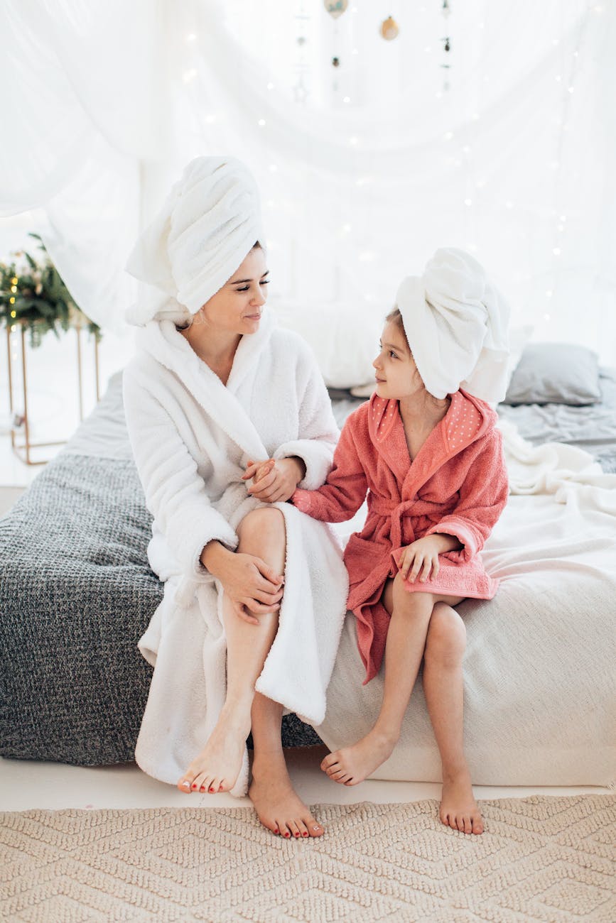 mother and daughter sitting on a bed in bathrobes