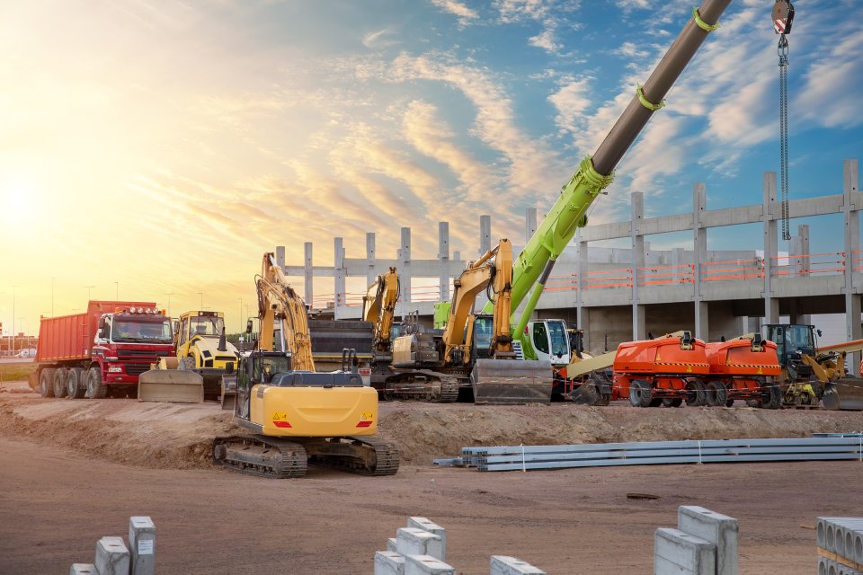 A construction site with a wide array of equipment parked on the dirt next to unfinished building.