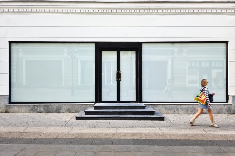 A woman with shopping bags walking past the windows of a large storefront—the windows are blank and ready for signage.