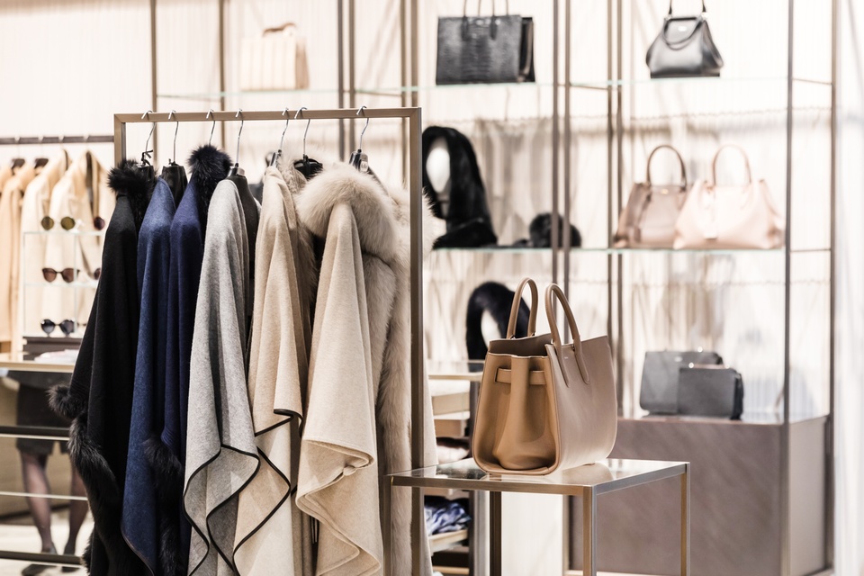 The inside of a luxury boutique. Coats are hung on a rack, purses and sunglasses are also on displays behind the rack.