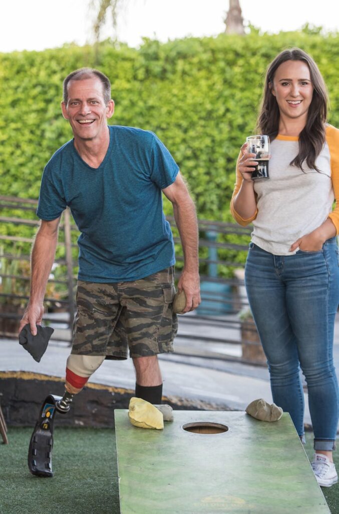 man playing cornhole beside a woman holding a drink