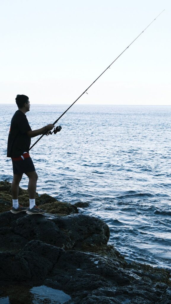 man fishing on rocky seashore at sunrise