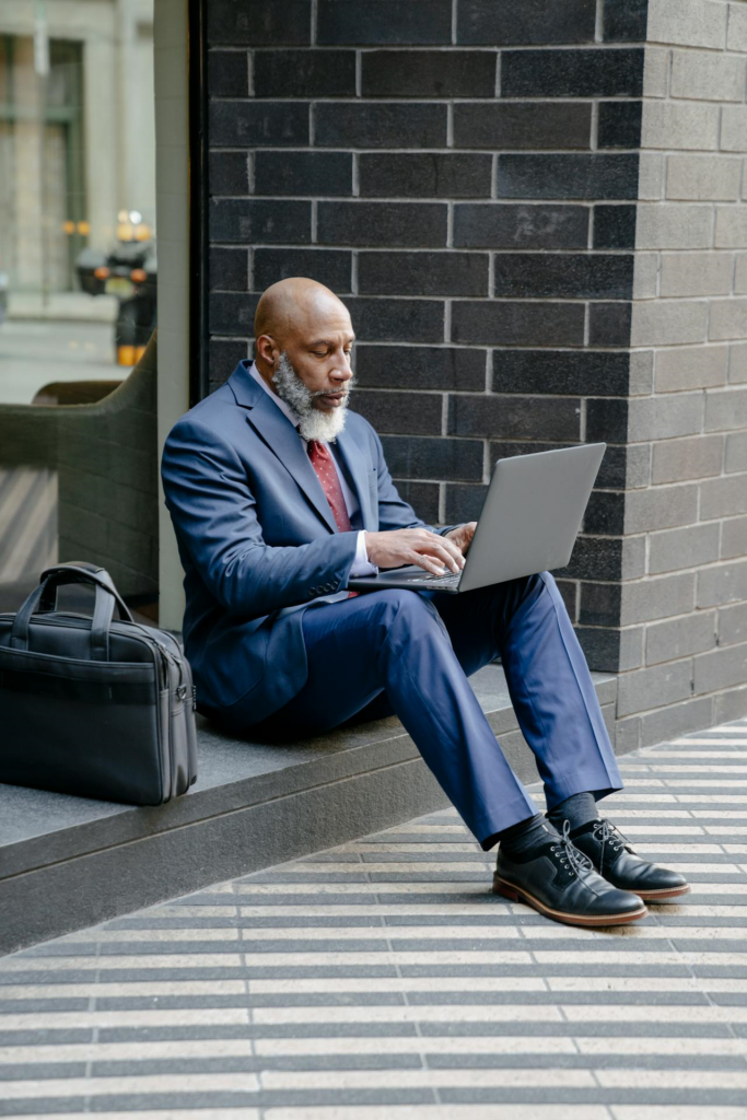 Man in Blue Business Suit Sitting on Concrete Floor while Using Gray Laptop