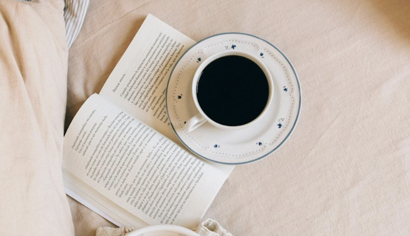 image - Lead Grow Develop - Business, Technology, Personal Development Open book on a beige bedsheet with a cup of black coffee on a patterned saucer.