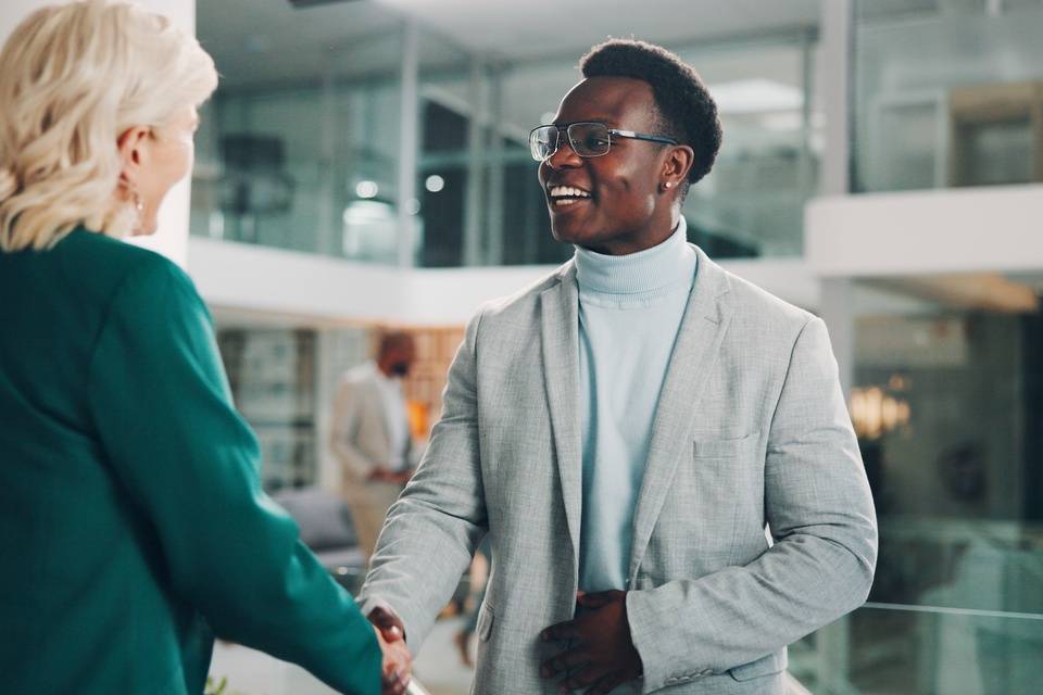a person shaking hands with an attendee at a trade show booth while other attendees stand near display counters. - Lead Grow Develop - Business, Technology, Personal Development a person shaking hands with an attendee at a trade show booth while other attendees stand near display counters.