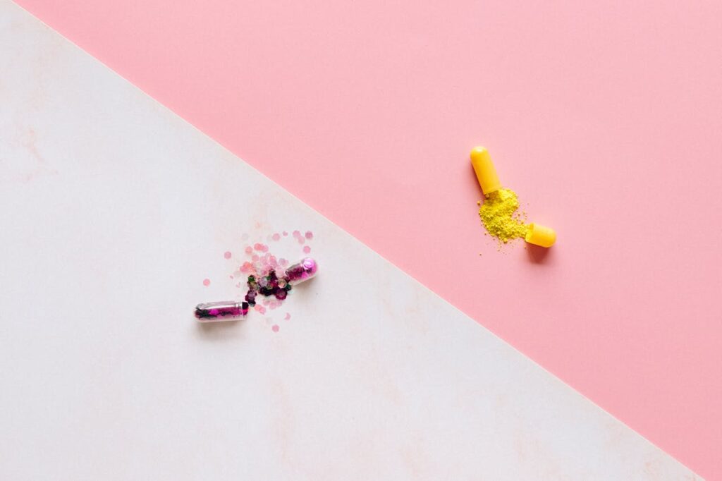 Vibrant capsules spilling colorful powder on a pastel pink and white split background.