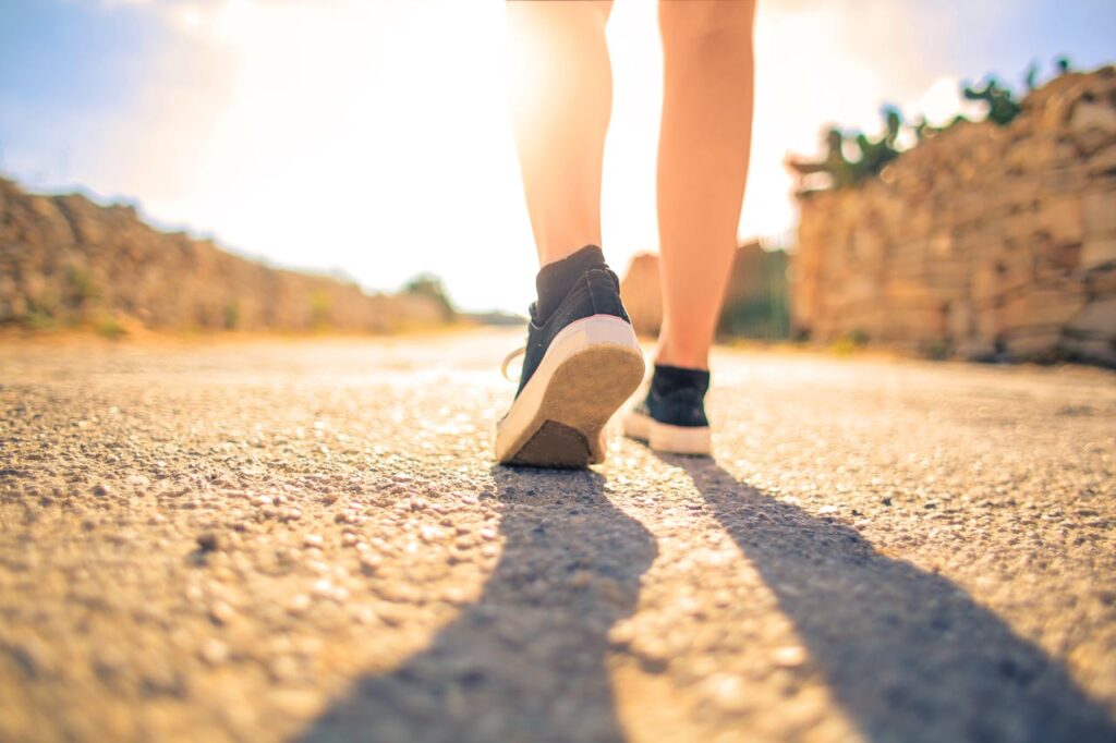 A woman walks down a sunlit path in summer, highlighting leisure and travel outdoors