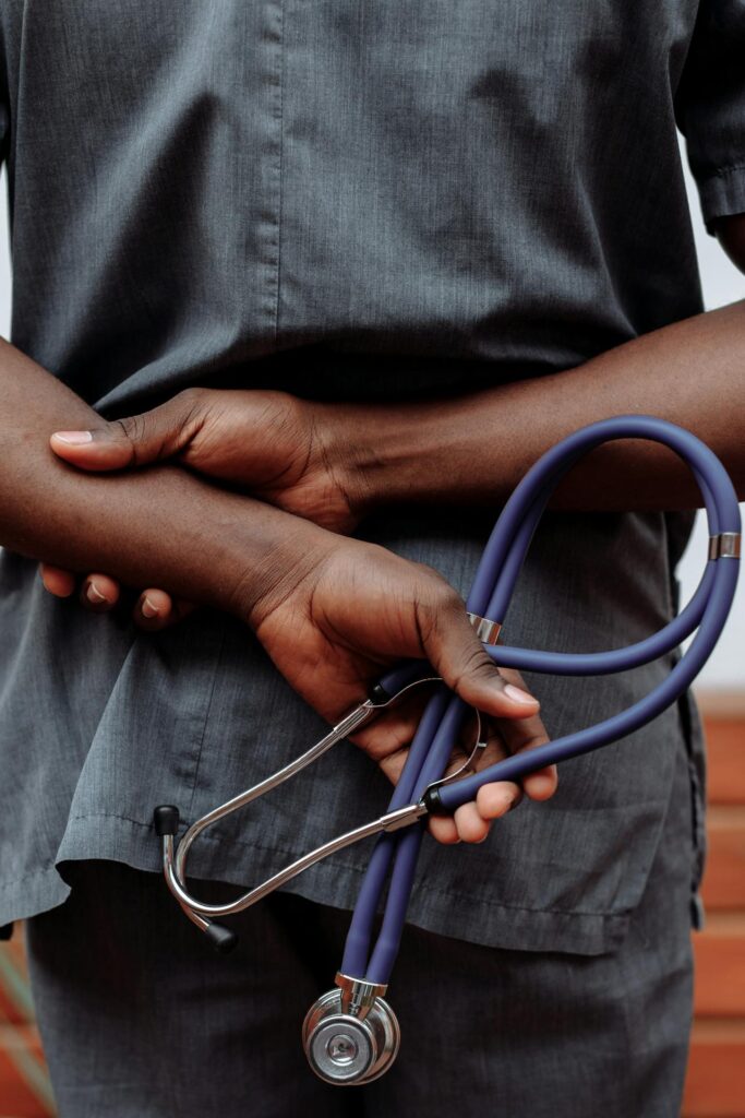 Medical professional in gray scrubs holding stethoscope behind back