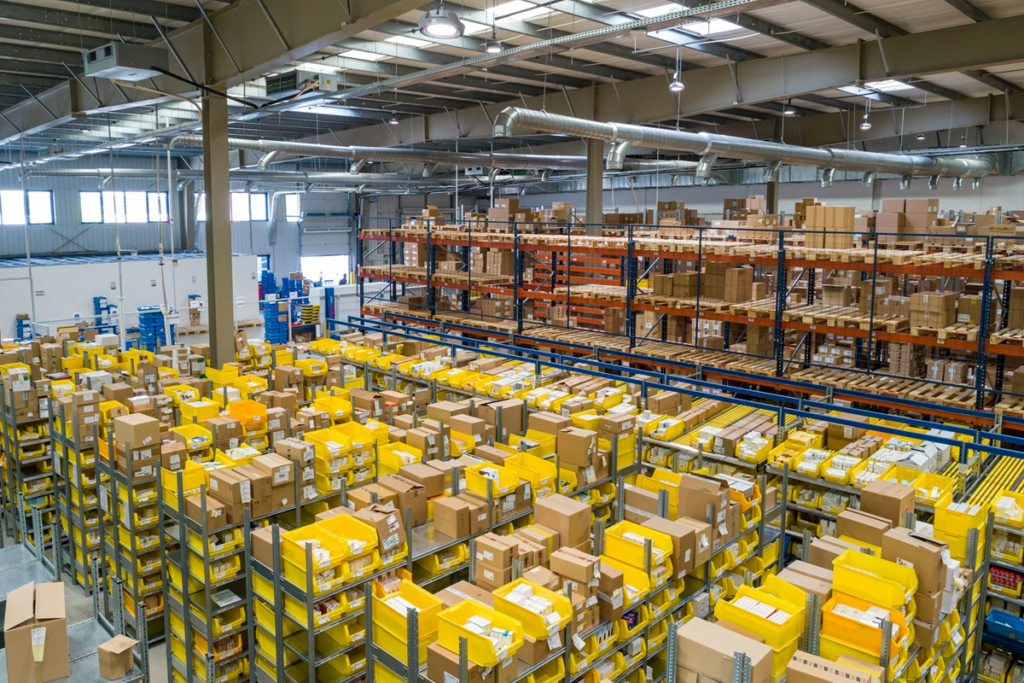 Warehouse warehouse with tall shelving filled with yellow bins and brown boxes, seen from a high vantage point during operation hours.
