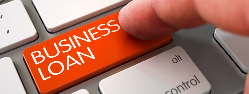 Orange key on a keyboard labeled 'BUSINESS LOAN' being pressed by a finger