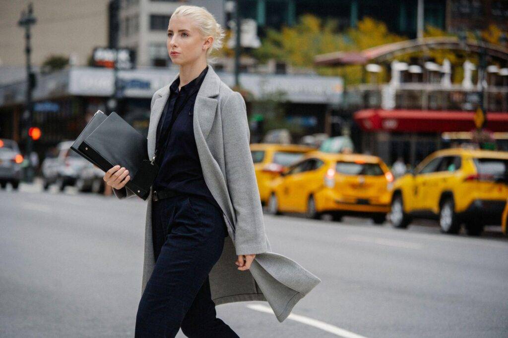 image - Lead Grow Develop - Business, Technology, Personal Development Businesswoman walking on a city street, carrying a black binder and gray coat in motion.