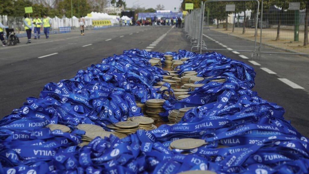 image - Lead Grow Develop - Business, Technology, Personal Development Pile of blue marathon ribbons and medals on a closed street, with barriers and event staff in the background. The Sevilla Marathon 2023 branding is visible on ribbons.
