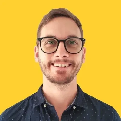 Josiah Roche - Connectively - Lead Grow Develop - Business, Technology, Personal Development Smiling man with short brown hair and black glasses, wearing a navy dotted shirt, against a bright yellow background.
