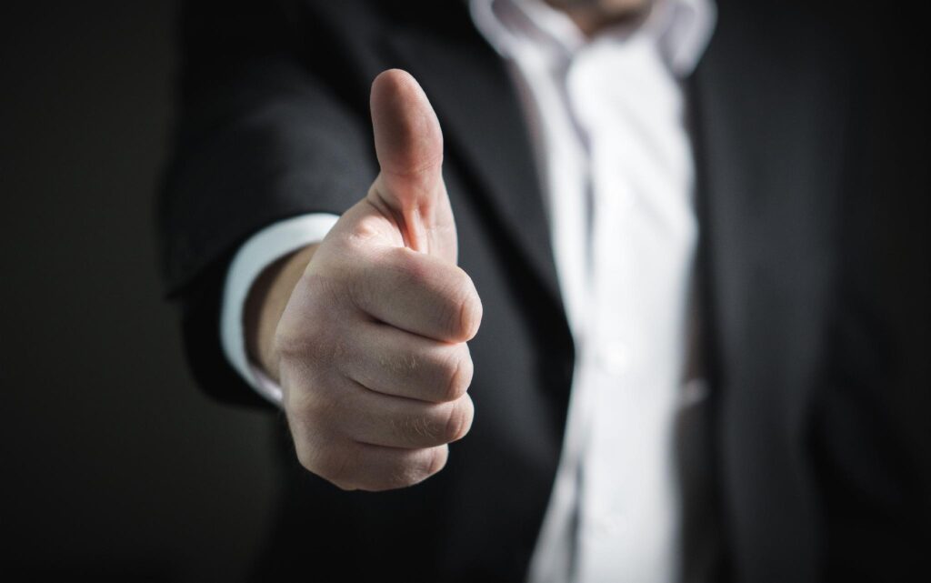 image - Lead Grow Develop - Business, Technology, Personal Development Close-up of a hand giving a thumbs-up, with a blurred business suit in the background.