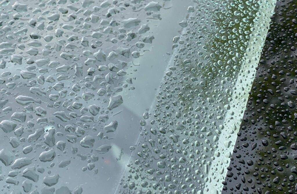 Close-up of numerous raindrops on a car windshield after rain.