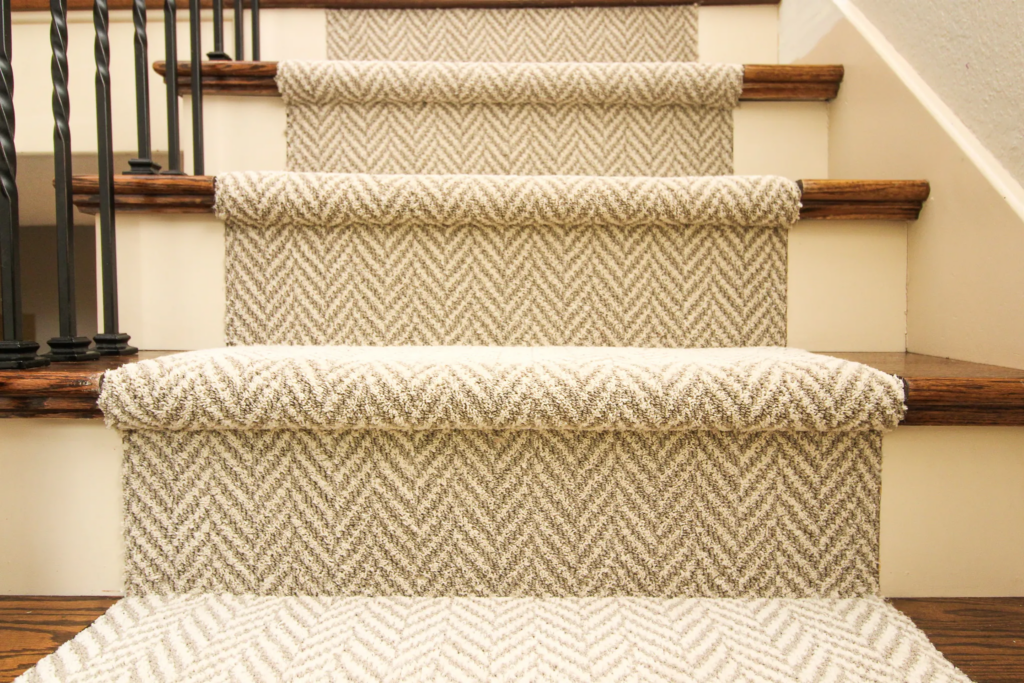 Carpeted staircase with beige chevron-patterned runners, wooden handrails, and black metal balusters