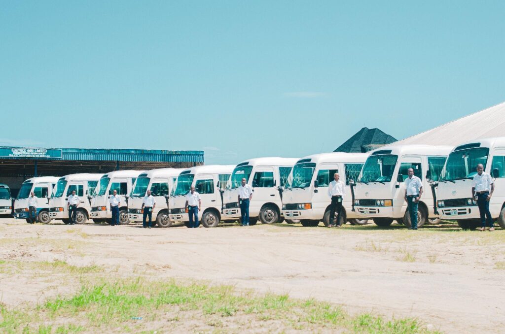 image - Lead Grow Develop - Business, Technology, Personal Development Line of white passenger vans parked side by side with people in white shirts standing in front under a clear blue sky.