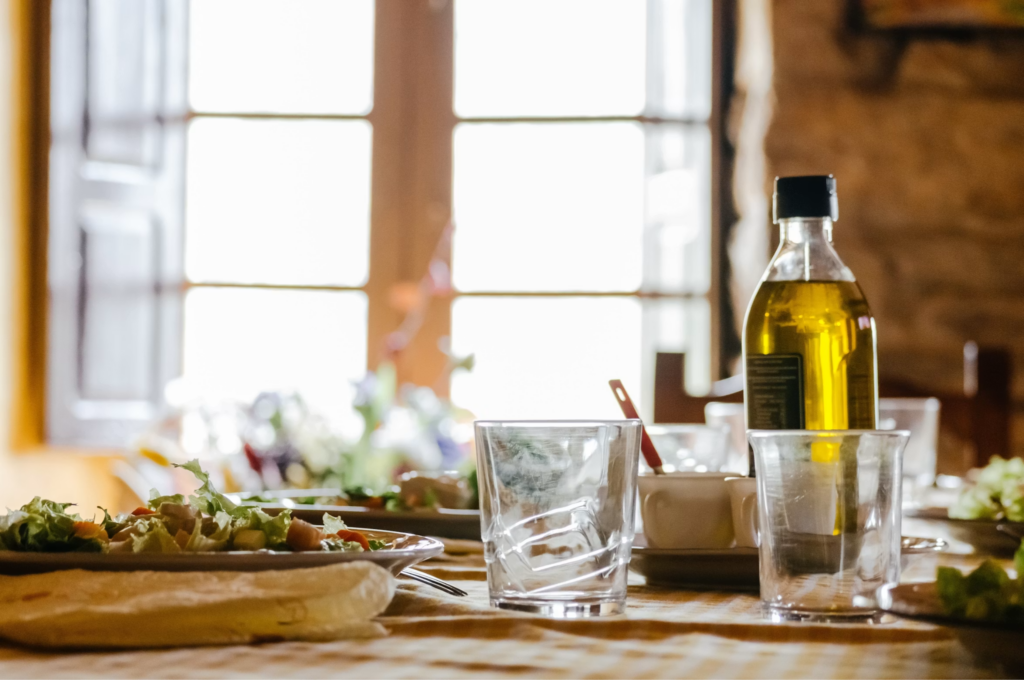 image - Lead Grow Develop - Business, Technology, Personal Development Table set for a meal: salad plate in the foreground, several glasses, and a bottle of oil on the right, with bright window light in the background.