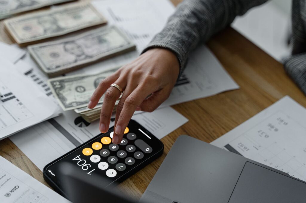 hand of a person using a calculator near cash money on wooden table