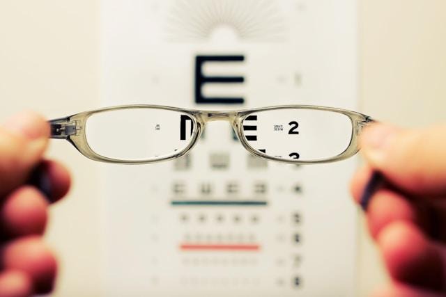 image - Lead Grow Develop - Business, Technology, Personal Development Glasses held in front of a vision chart during an eye exam, focusing on clear letters in the foreground