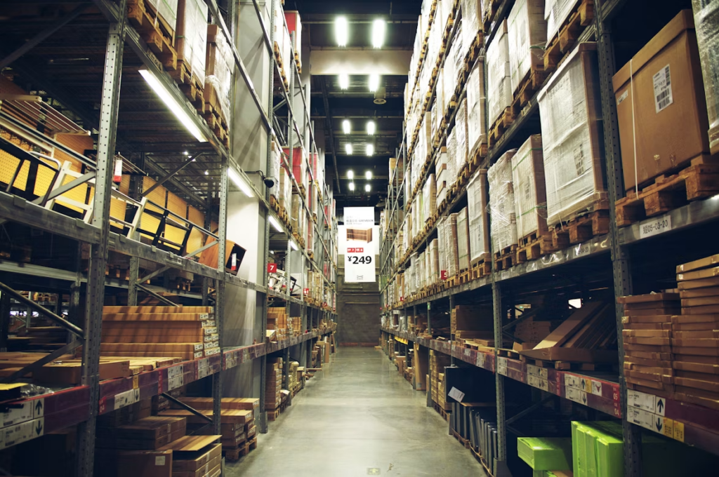 image - Lead Grow Develop - Business, Technology, Personal Development Long warehouse aisle with tall metal shelves stocked with boxes and pallets, illuminated by fluorescent lights.
