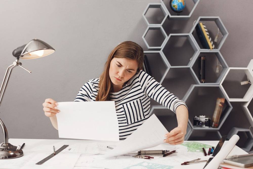 image - Lead Grow Develop - Business, Technology, Personal Development Woman in a striped shirt reviewing architectural plans at a desk with drafting tools in a modern workspace